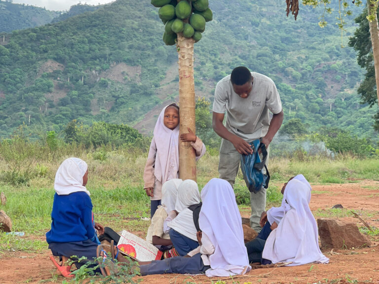 Children under a pawpaw tree playing with forest focus team